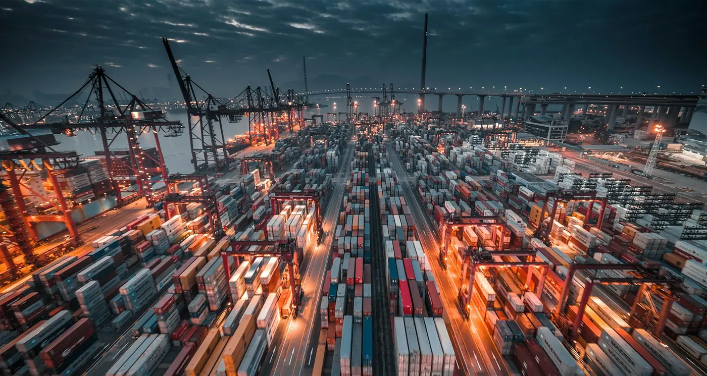 A container terminal at dusk, with stacked containers and quay cranes.
